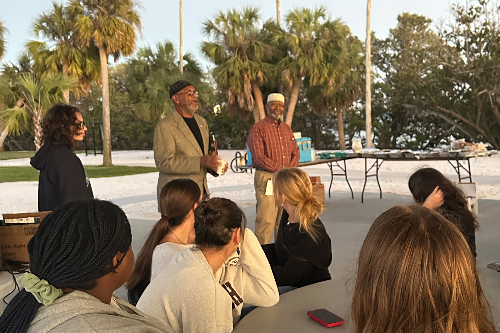 Two gentlemen speak before a crowd under an outdoor pavilion