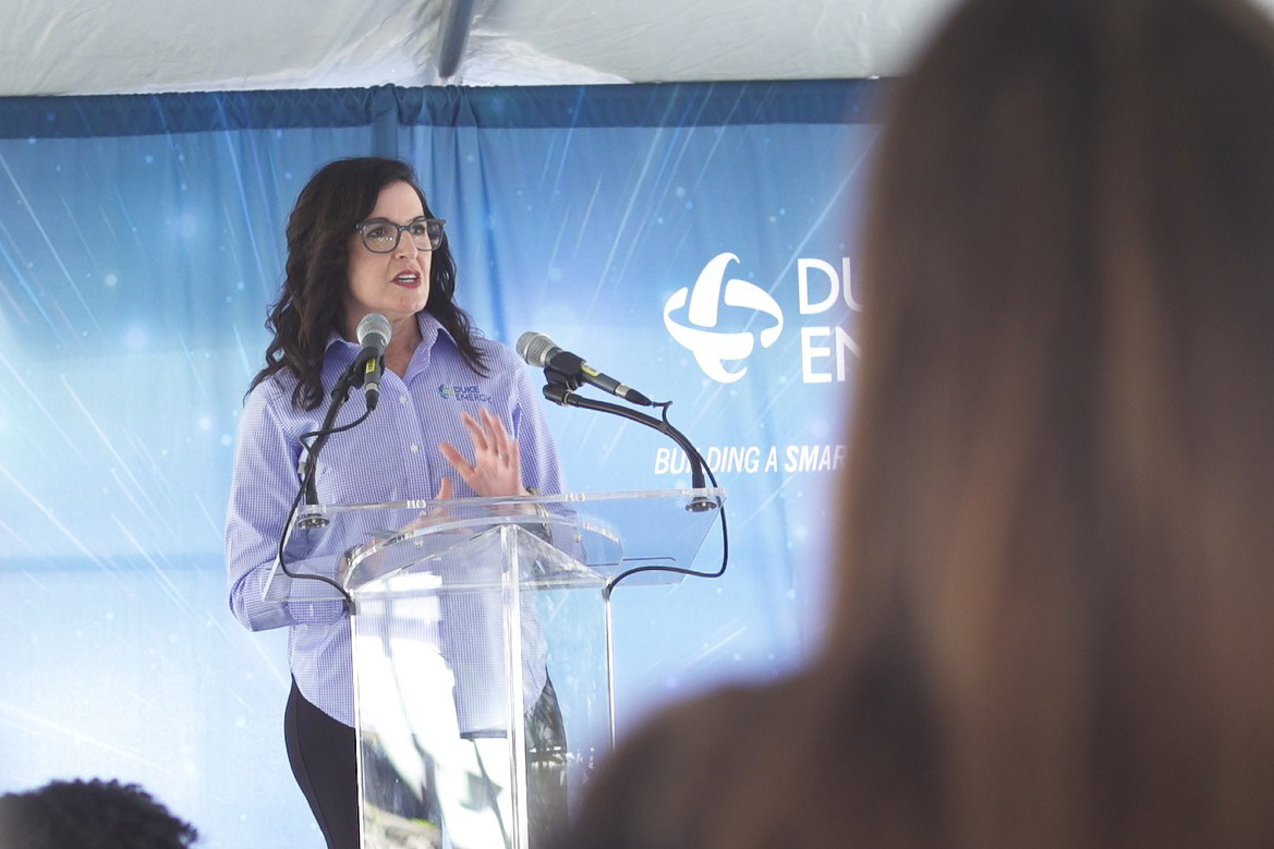Woman at glass podium in front of sign with words Duke Energy