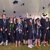 Large group of students standing under a tall tent toss their caps into the air