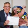 Student holds cat wearing graduation cap next to president who holds a certificate