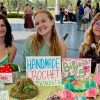 Three students seated at a table with signs that read HANDMADE CROCHET THINGS