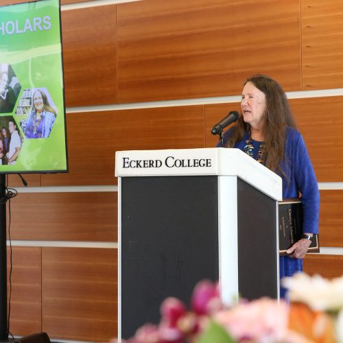 Woman at podium holding plaque and standing by monitor that reads FORD SCHOLARS
