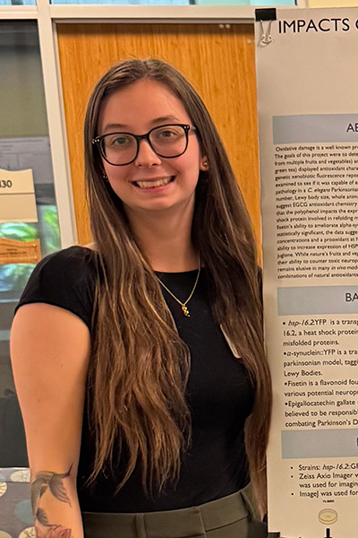 Student wearing glasses stands next to scientific poster