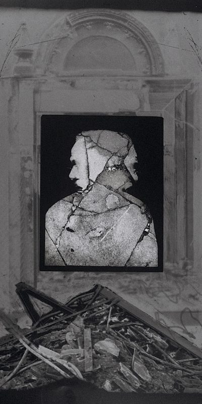 Black and white photo of interior of old room with rubble on ground a cracked bust in the window