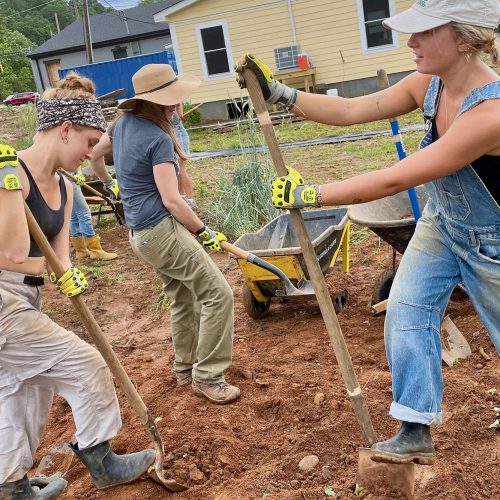 Student volunteers use shovels to remove red clay from the land