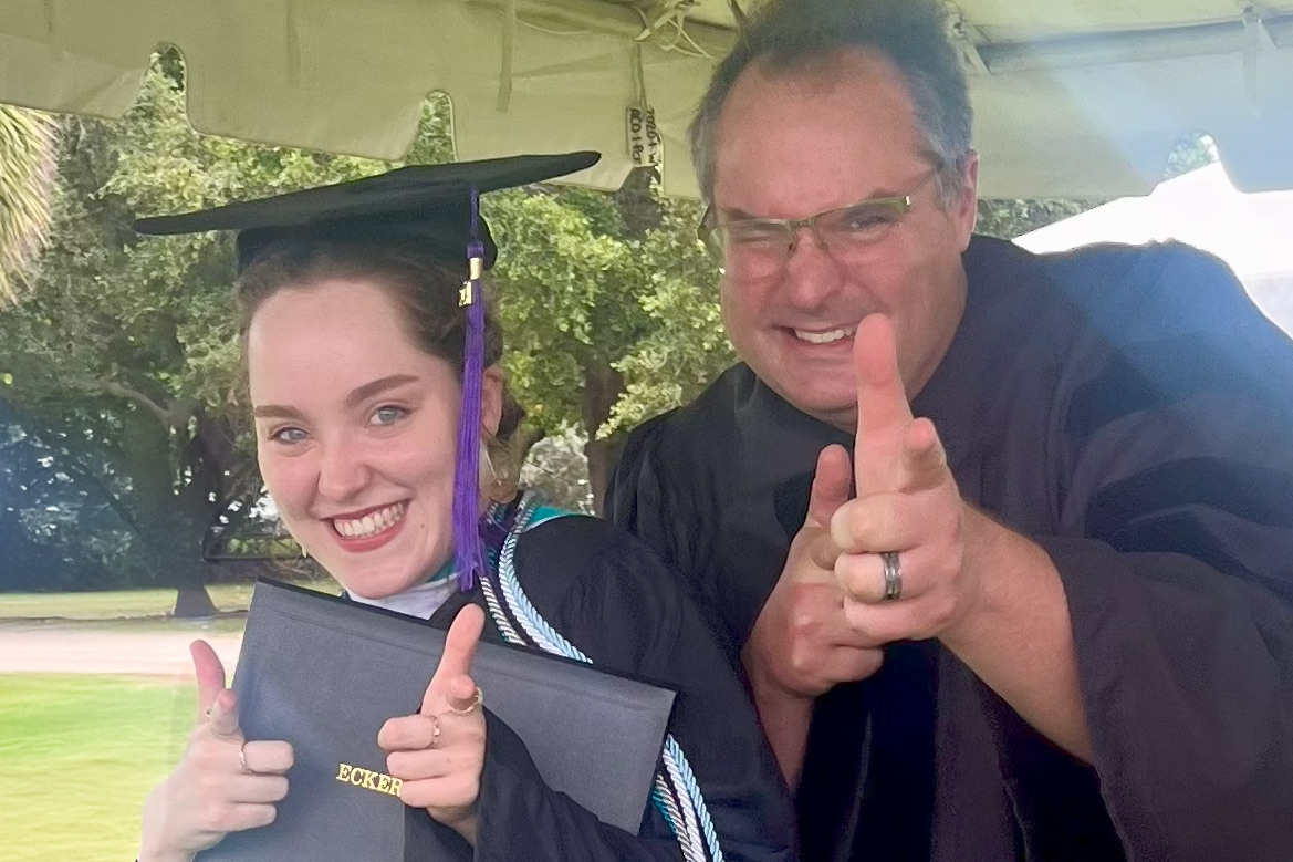 Student in grad cap stands next to professor in gown as they both pose for camera