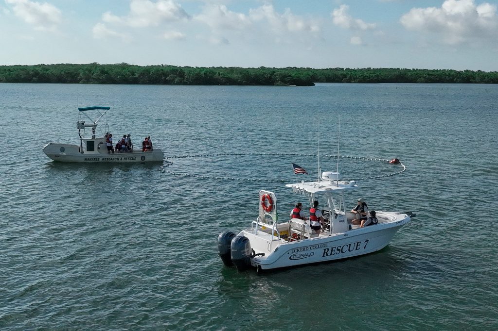 Side view of two boats in the water after extending a long line that forms a large circle in the water