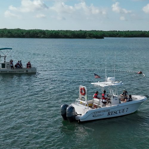 Side view of two boats in the water after extending a long line that forms a large circle in the water