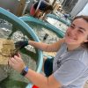 Young woman squats beside a water tank holding crabs