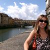 Student wearing purse and sunglasses stands in front of river passing through an old European city