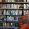 Shelves of books and a blurred image of a student wearing a backpack walking by