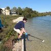 Two students wearing gloves use equipment to sample water at a saltwater creek