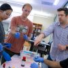 Professor and students in protective eyewear in a lab point to vials on a table