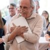 Professor smiles humbly while holding laptop to his chest