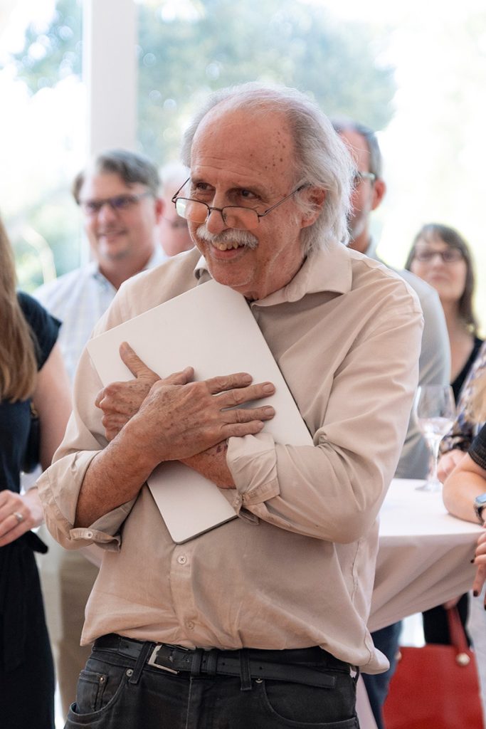 Professor smiles humbly while holding laptop to his chest