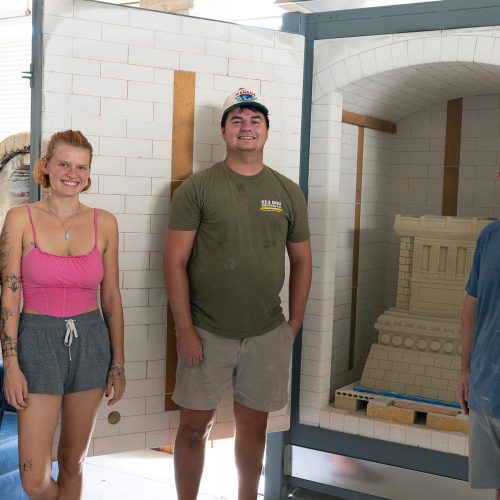 Three students stand side by side a professor with a clean kiln behind them