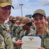 Young man in fatigues holding certificate presented to him by another member of the military