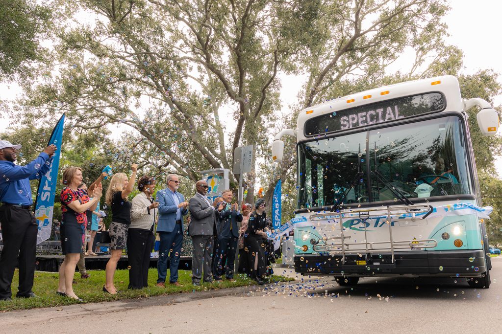 A line of people cheer as a bus rides through a ribbon