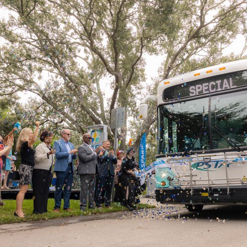 A line of people cheer as a bus rides through a ribbon
