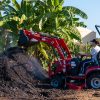 Student sits atop a red tractor as it dumps dirt onto a large pile