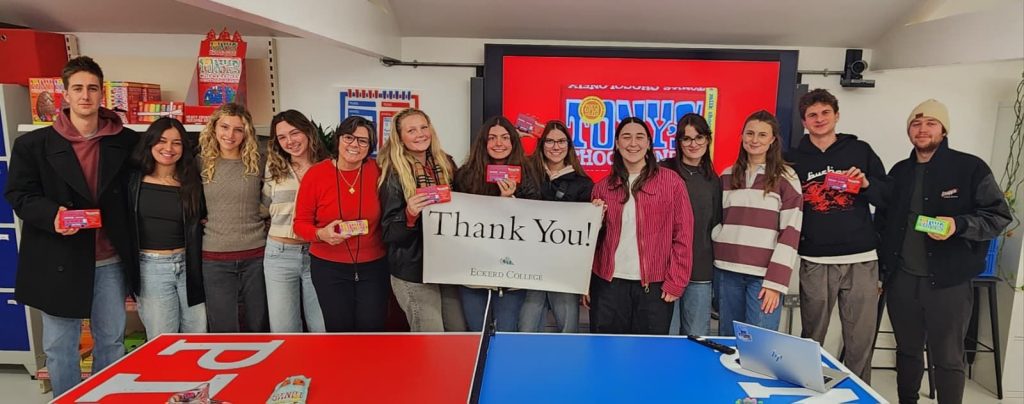 Group of students stand with professor in a factory holding a sign that reads THANK YOU