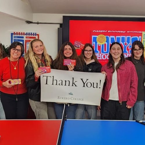 Group of students stand with professor in a factory holding a sign that reads THANK YOU