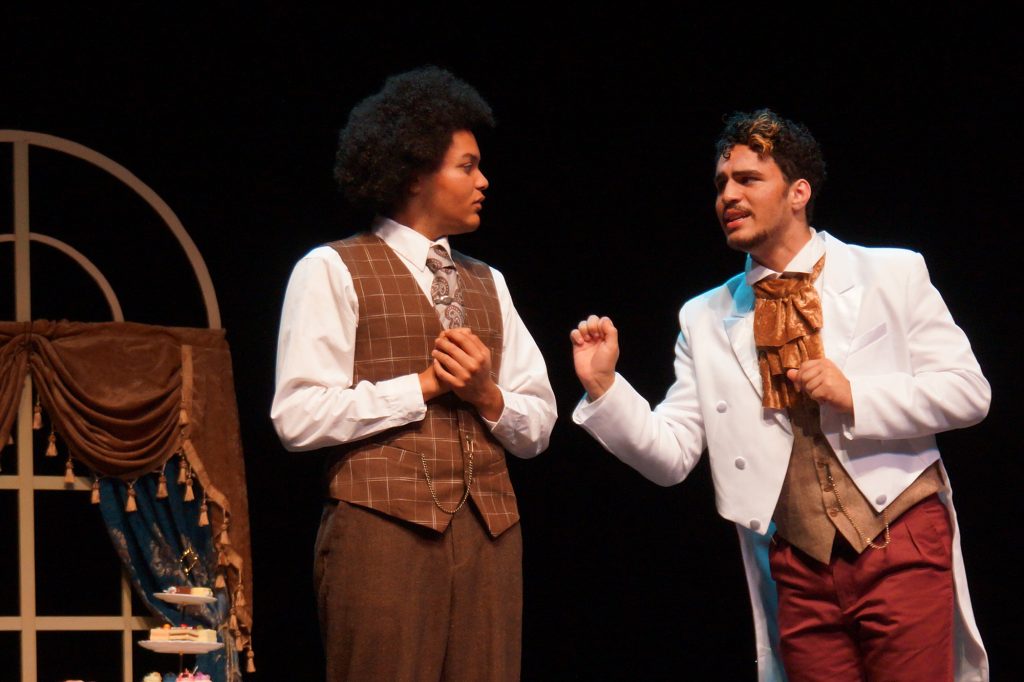 Two actors talking to one another on stage dressed in 1890's attire