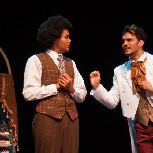 Two actors talking to one another on stage dressed in 1890's attire