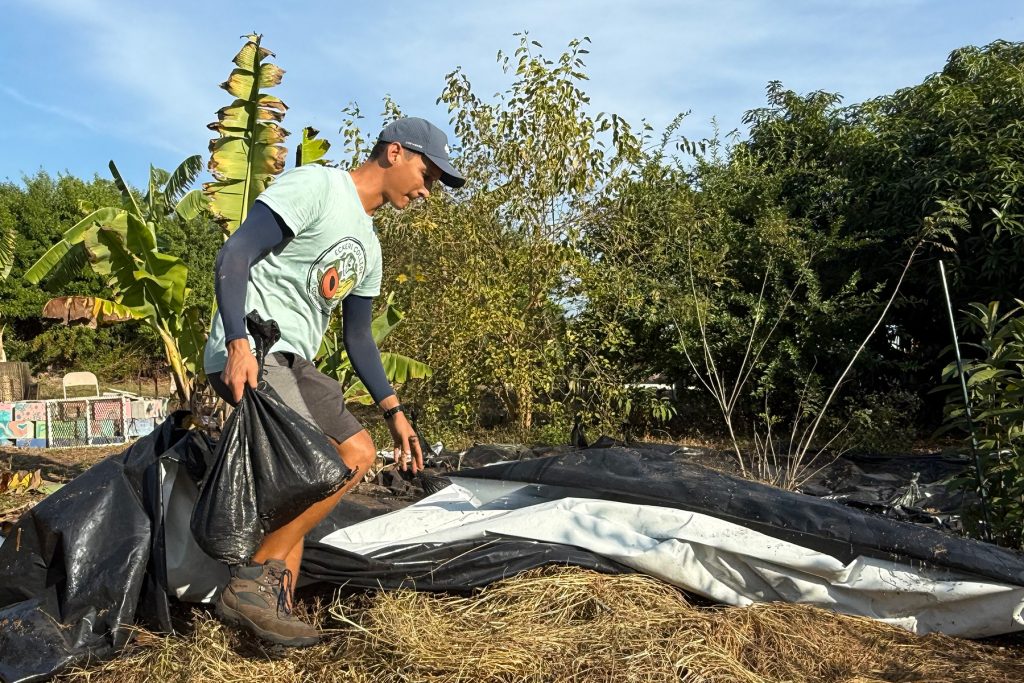 Young man in boots and shorts and cap lays out a black tarp on the ground
