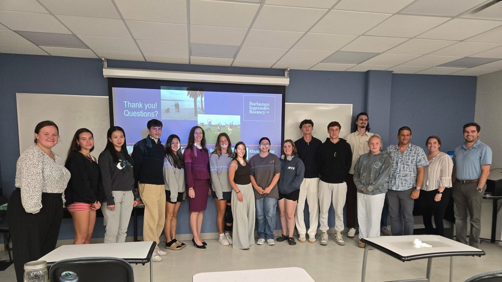 Large group of students and staff stand side to side in front of a projector