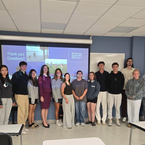 Large group of students and staff stand side to side in front of a projector