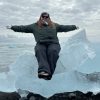 Student in snow gear and sunglasses sits on a small iceberg