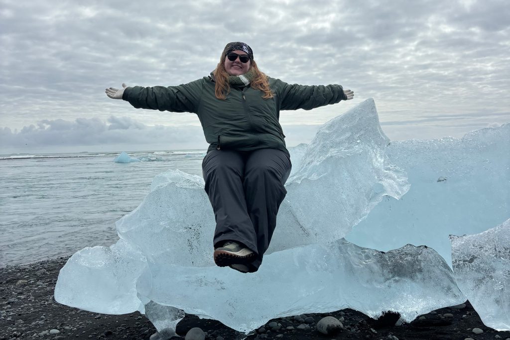 Student in snow gear and sunglasses sits on a small iceberg