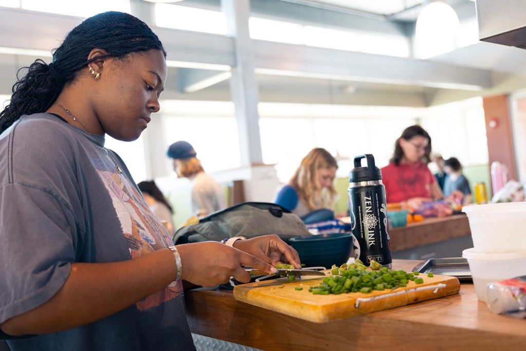 Student chopping food on cutting board in a large room