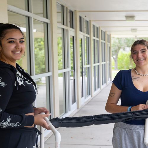 Two students stand together holding a bird perch