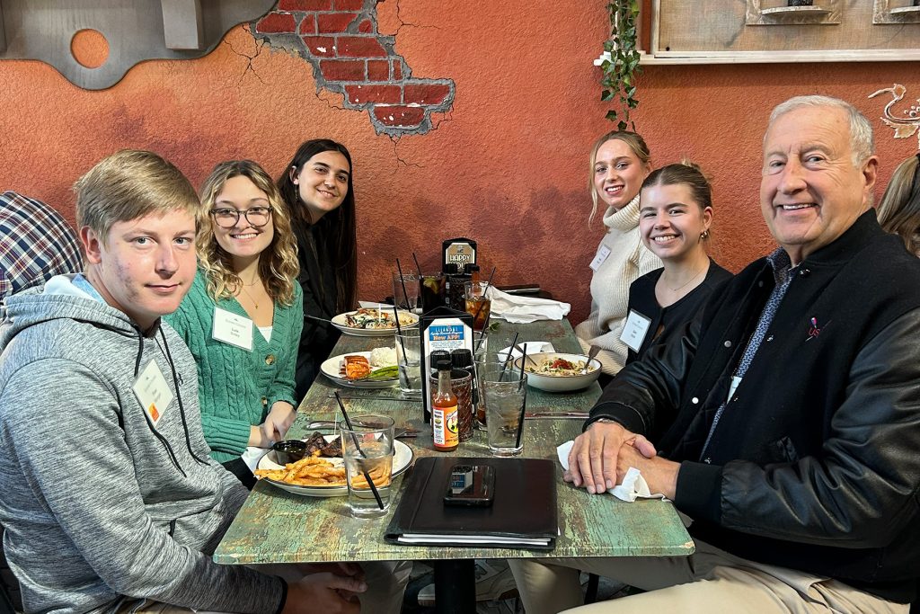 Group of five students sit with an older gentleman at a restaurant table