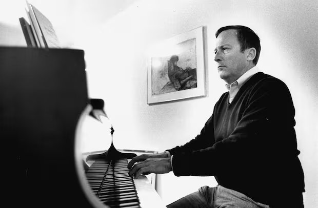 Black and white photo of a man in sweater playing piano