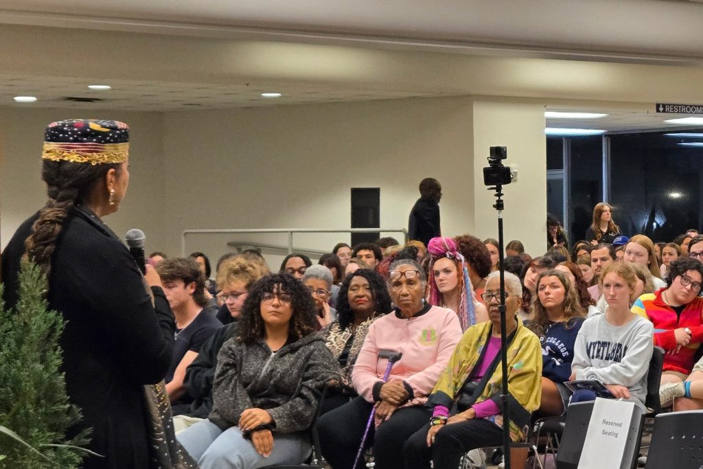 Woman wearing hat stands in foreground while addressing an audience
