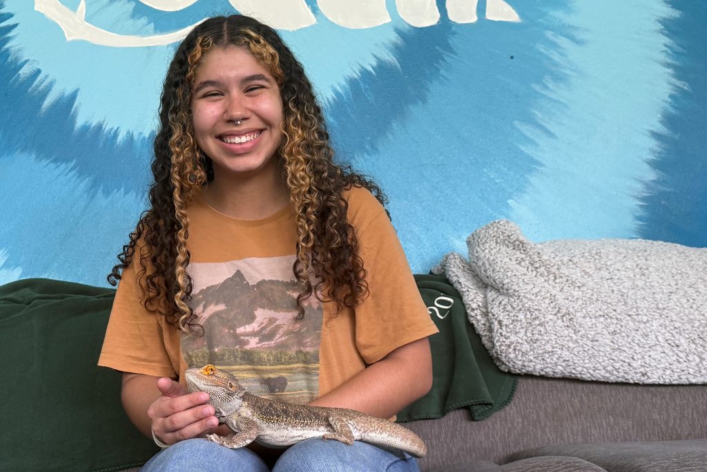 Student sits on a couch with a bearded dragon in her lap
