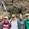 Five students stand arm in arm in front of a small waterfall