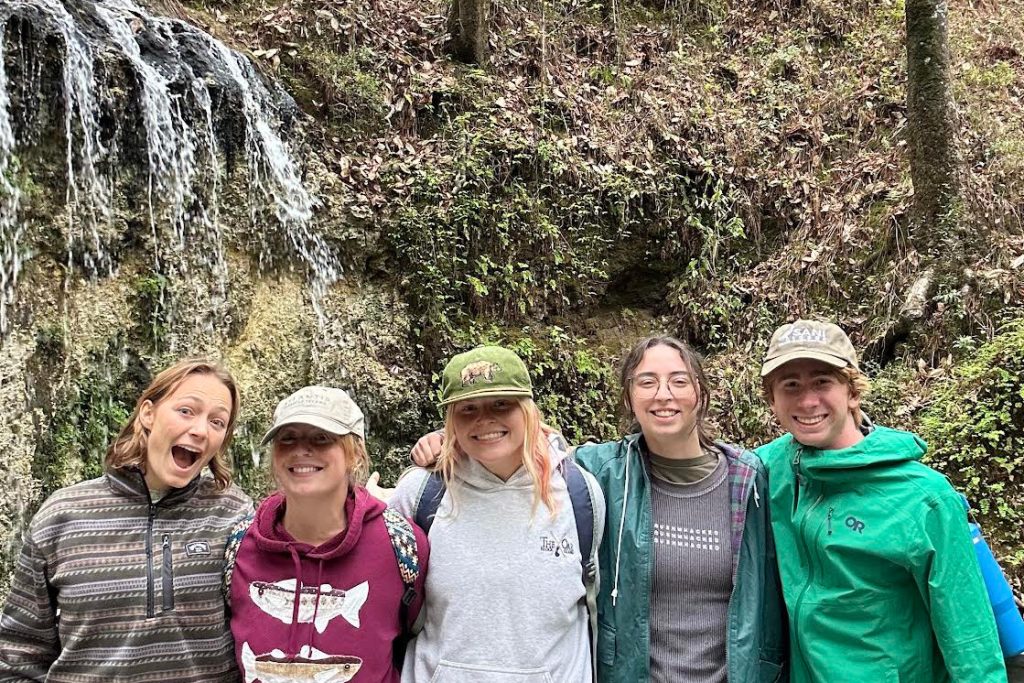 Five students stand arm in arm in front of a small waterfall