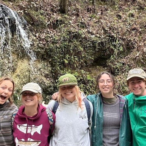 Five students stand arm in arm in front of a small waterfall
