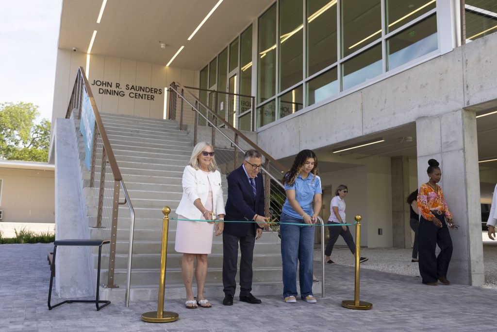 Three people at the bottom of a staircase cutting a ribbon.