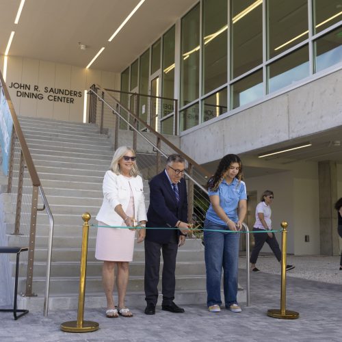 Three people at the bottom of a staircase cutting a ribbon.