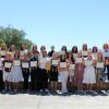 A group of students stand outside in front of a pond displaying framed certificates.