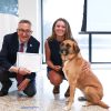 President Annarelli awarding an honorary degree to a sitting dog as the dog's smiling owner looks on.
