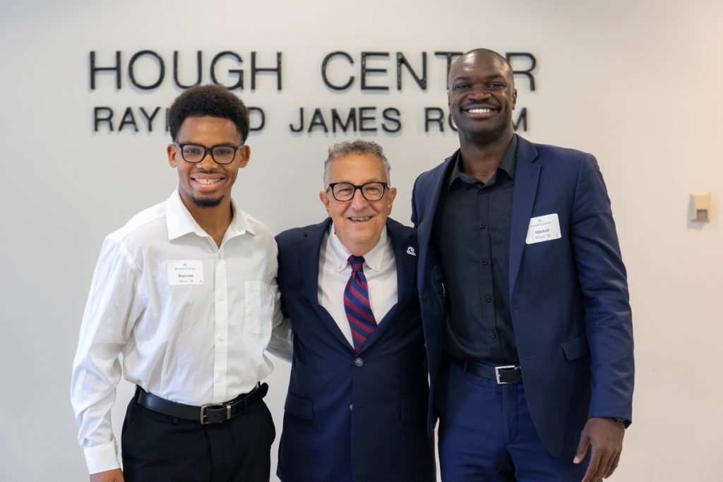 Three men pose together for a photo in front of a white wall.