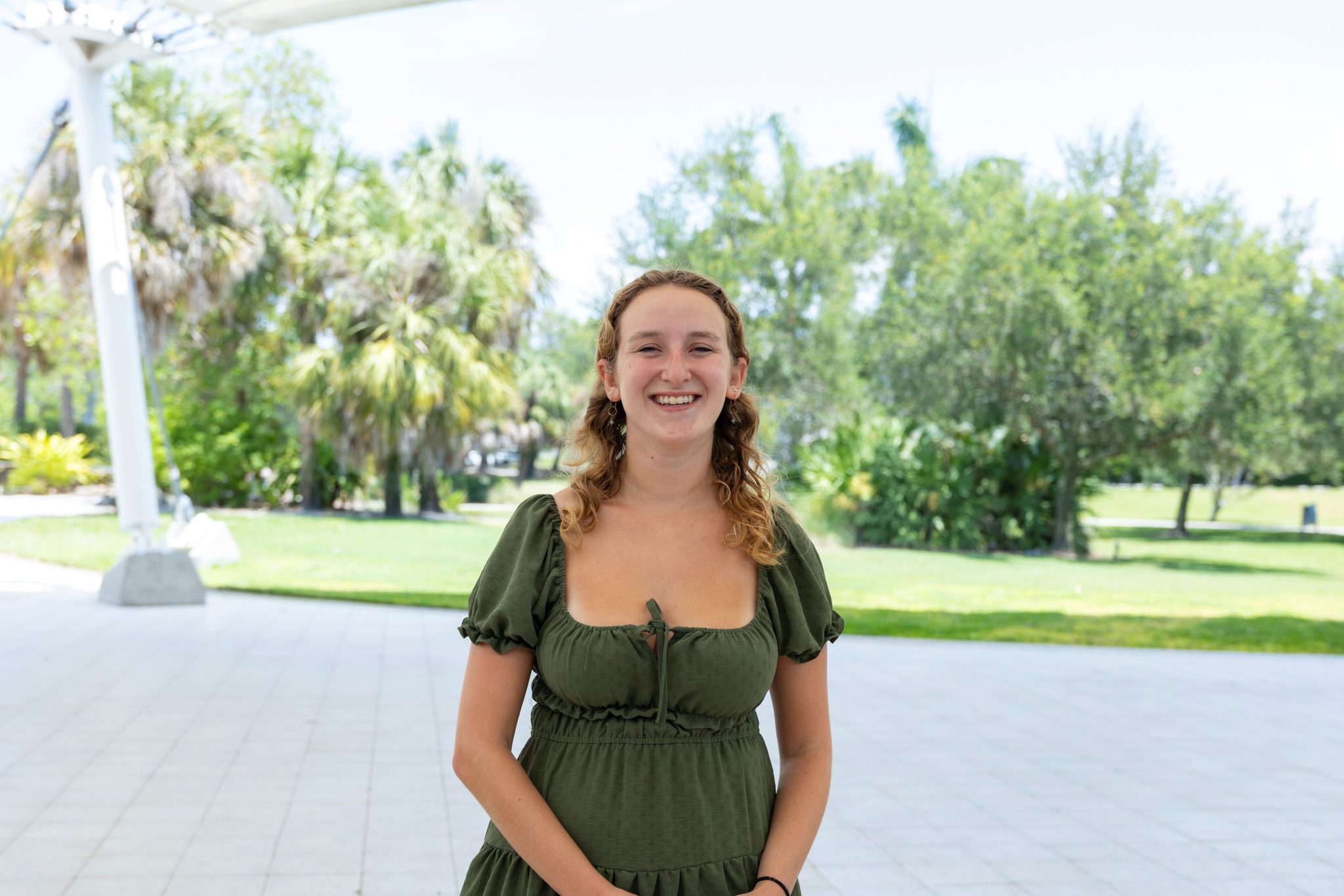 A girl posing for a photo outdoors in the shade.