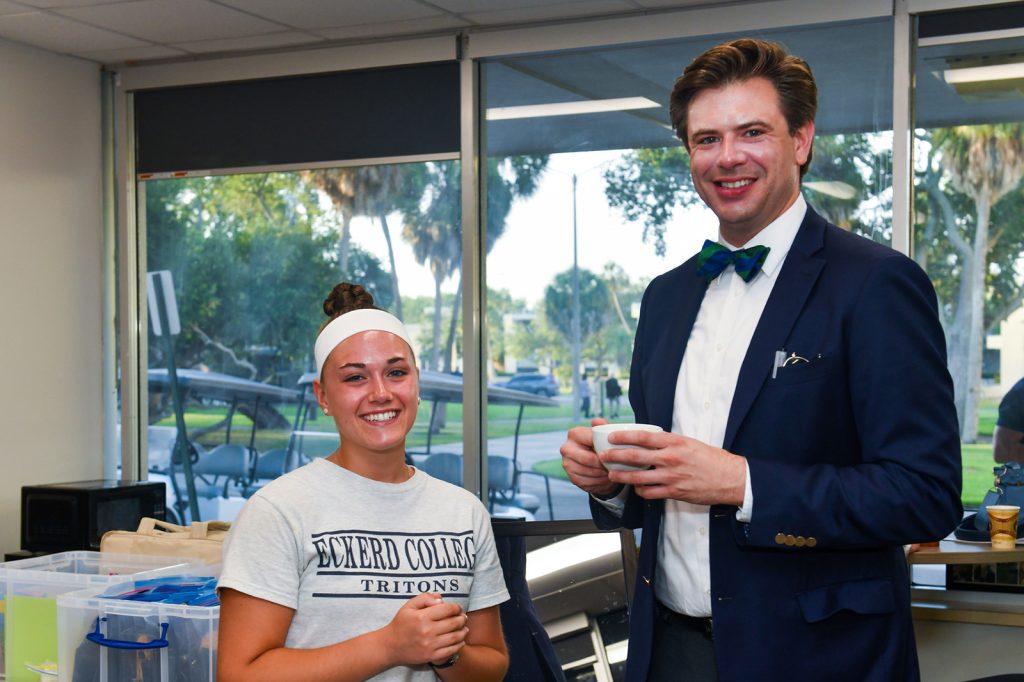 Gentleman in bow tie and jacket stands next to a student in a shirt that reads ECKERD TRITONS