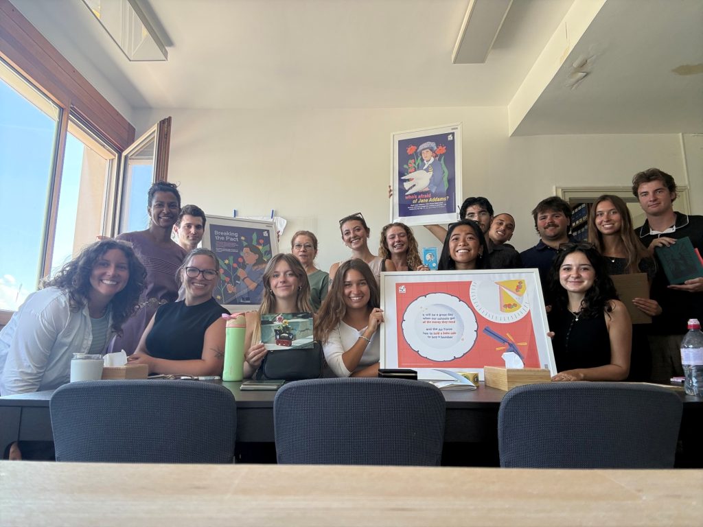 A group of around a dozen people sit at a table smiling and holding up a framed display.